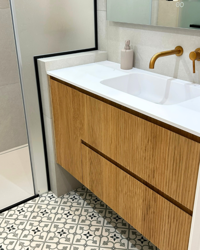 Baño de la reforma Dolors con mueble suspendido de madera, encimera blanca y grifería dorada empotrada