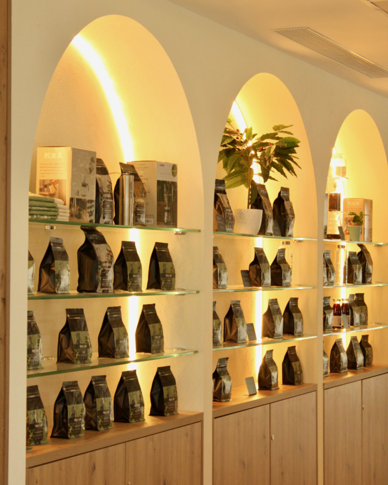Estanterías de la Cafetería Sirirí bajo arcos iluminados, con paquetes de café de especialidad